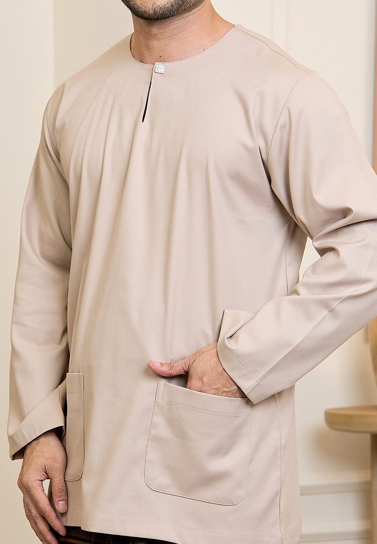 Man wearing a nude color long-sleeve baju melayu teluk belanga with a pocket against a neutral background