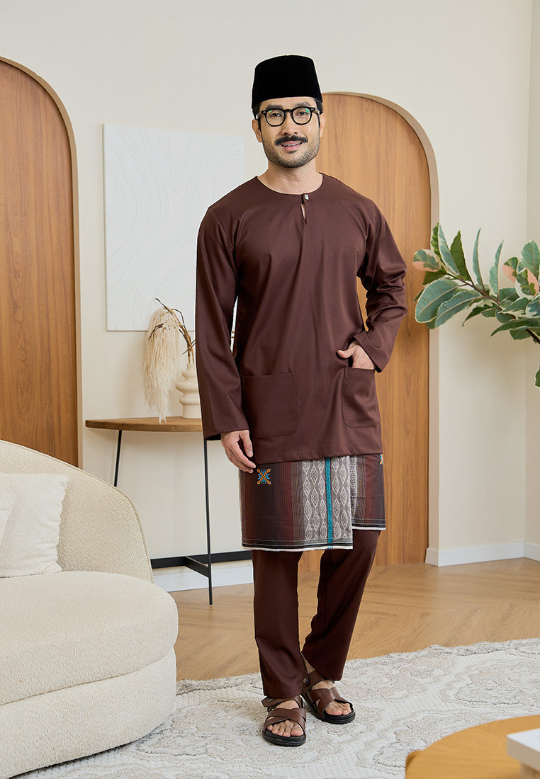 Man wearing a rich brown traditional baju melayu teluk belanga outfit in a modern living room