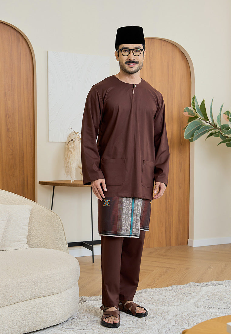 Man wearing a rich brown traditional baju melayu teluk belanga outfit in a modern living room setting