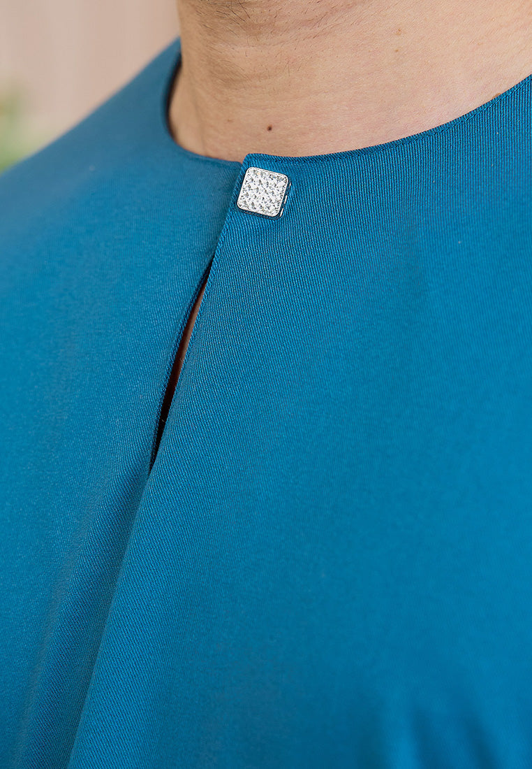 Close-up of a teal blue garment of baju melayu teluk belanga with a decorative magnetic button on a blurred background